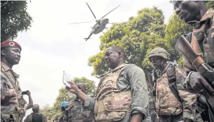  ?? AFP ?? Central African Republic Prime Minister Firmin Ngrebada, centre, talks to his troops, as a Russian made support helicopter flies over, on the road between Boali and Bangui on Sunday.