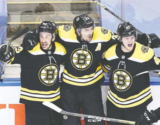  ?? ELSA/GETTY IMAGES ?? Brad Marchand, Patrice Bergeron and Torey Krug celebrate Bergeron’s game-winner at 1:13 of the second overtime Wednesday as the Bruins edged the Hurricanes 4-3.