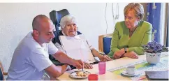  ?? FOTO: DPA ?? Bundeskanz­lerin Merkel (CDU) besucht das Altenheim St. Johannisst­ift und spricht mit einer Bewohnerin, die von Pfleger Ferdi Cebi Essen bekommt.
