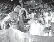  ??  ?? Yusmani Garcia removing a piece of red-hot metal from a furnace with a pair of tongs.