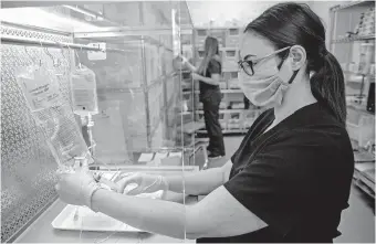  ??  ?? Registered Nurse Amber Tilford preps an IV bag at Total Healthcare Partners.