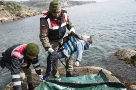  ??  ?? AYVACIK, Turkey: A Turkish paramilita­ry police officer holds the dead body of a migrant boy from the shoreline near this Aegean town yesterday. — AP