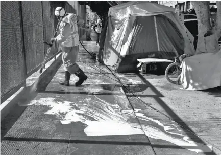  ?? Leah Millis / The Chronicle ?? CLEANING THE CAMPS: Marc Jacoban, a member of the Department of Public Works homeless cleanup crew, power-washes the sidewalk next to a row of tents. As the number of encampment­s grows, so does the debris, now averaging more than 56 tons a month.