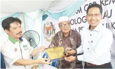  ??  ?? Zaini (right) signing a plaque to signify the launch of KeTTHA’s CSR programme at Kampung Kibagu, Menggatal as Saidi (centre) looks on.