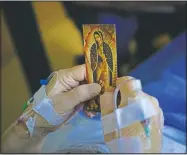  ?? (AP/Jae C. Hong) ?? A patient holds an Our Lady of Guadalupe card in his bed while talking to chaplain Nancy Many at Providence Holy Cross Medical Center in the Mission Hills section of Los Angeles on Jan. 9. As families are barred from visiting loved ones to curb the disease’s spread, chaplains often are there to act as surrogates, holding the hands of the dying, praying with them and carrying iPads into hospital rooms to provide a real-time connection with grieving families.