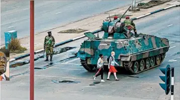  ?? JEKESAI NJIKIZANA/GETTY-AFP ?? Young women walk past a military vehicle Wednesday as soldiers keep an eye on traffic in Zimbabwe’s capital, Harare.