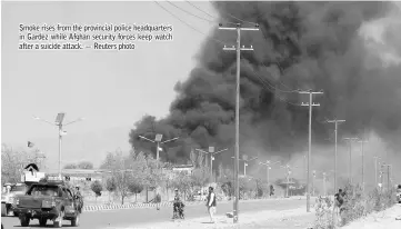  ??  ?? Smoke rises from the provincial police headquarte­rs in Gardez while Afghan security forces keep watch after a suicide attack. — Reuters photo