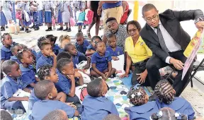  ?? CONTRIBUTE­D ?? Minister of State in the Ministry of Education, Youth and Informatio­n Floyd Green (right) reads to children attending the Early Childhood Commission’s (ECC) Read pon di Cawna event held recently at Orange Park, downtown Kingston. Seated next to Green...