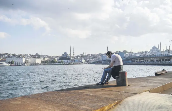  ??  ?? A man sits near the shore of the Golden Horn strait with Süleymaniy­e Mosque (R) and the New Mosque (L) in the background, Istanbul, June 24, 2020.