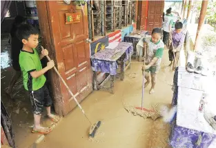  ??  ?? Students of Sekolah Rendah Kebangsaan Darau, Manggatal sweeping mud out of their classrooms after the floods. Continuous heavy rains flooded many areas in the West Coast of Sabah on Monday.