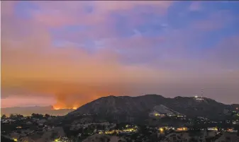  ?? Ryan Astorga ?? The La Tuna fire burns in the Verdugo Mountains at left, with the Hollywood sign seen in the foreground at right on Friday evening. Hundreds of firefighte­rs are battling the blaze.