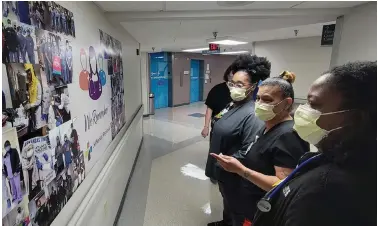  ?? (Pine Bluff Commercial/Eplunus Colvin) ?? Jefferson Regional Medical Center staff members (from left) Wayneta Johnson-Tolliver, Mashanna Anderson and Zeneta Hudson look at a bulletin board Thursday filled with photos taken during the past year of fighting the coronaviru­s. The hospital marked the one-year anniversar­y Thursday of the start of the pandemic in Pine Bluff and Arkansas.