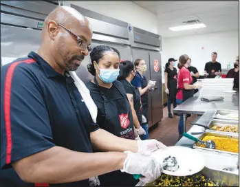  ??  ?? Lead cook Bobby Grayson, left, shows volunteer Aziza Adem how much food to serve.