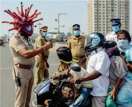  ??  ?? Protezioni anti pandemia
Un poliziotto con un casco a forma di virus ferma una famiglia durante il coprifuoco a Chennai in India (Foto Sankar/afp)
