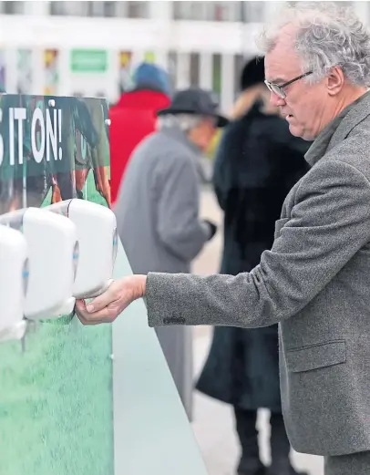  ?? Picture: PA. ?? Racegoers use hand sanitiser to keep their hands clean on day one of the Cheltenham Festival at Cheltenham Racecourse.