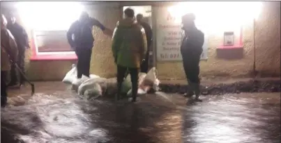  ??  ?? Residents in Coachford pitch in as flood waters running down the street threaten Mag’s Chipper on December 28, 2015 - flooding which was not considered in the OPW assessment of the region in 2016.
