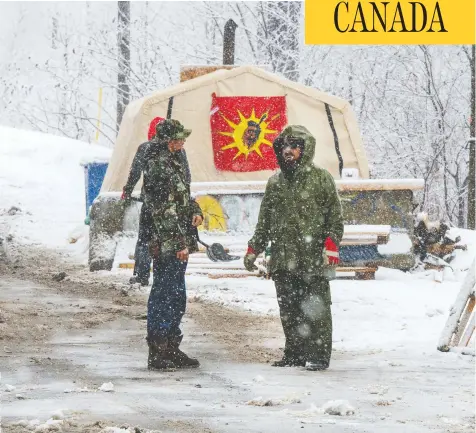  ?? RYAN REMIORZ / THE CANADIAN PRESS ?? Protesters stand near the entrance of a blockade of the rail line in Kahnawake Mohawk Territory, near Montreal, on Thursday.