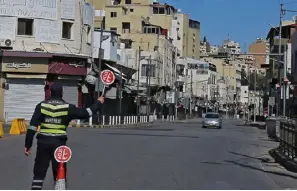  ??  ?? شرطي يحمل لافتة في شارع شبه مهجور في العاصمة الأردنية عمان
