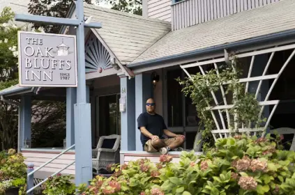  ?? Lauren Justice, © The New York Times Co. ?? Erik Albert sits on the porch of his The Oak Bluffs Inn, in Oak Bluffs, Mass. Black vacationer­s have flocked to Oak Bluffs for more than 100 years.