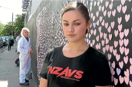  ??  ?? Tara Jackson with the wall of hearts protest against animal testing. The man in the overalls is the contractor engaged to take the hearts down.