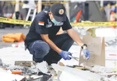  ??  ?? A forensic investigat­or collects samples of recovered belongings believed to be from the crashed Lion Air flight JT610.