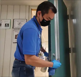  ?? DAVE ANGELL — FOR THE MACOMB DAILY ?? Rolando Delos Santos, a custodian at the Utica Community Schools, cleans a doorknob after school at Bemis Junior High in Sterling Heights. Cleaning standards, with a focus on touch points, has increased at public schools during the COVID-19pandemic.