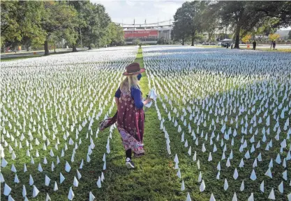  ?? JACK GRUBER/USA TODAY ?? “IN AMERICA: How Could This Happen” project artist Suzanne Firstenber­g walks through the installati­on on the DC Armory Parade Ground on Oct. 23, 2020, in Washington, D.C. At the time, the project honored each of the 225,000 lives lost in the U.S. from COVID-19 with a white flag. Another 775,000 Americans have been killed by the disease since then.