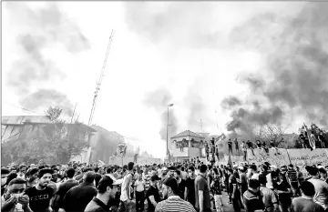  ?? — AFP photos ?? Iraqi protesters gather outside the burnt-down local government headquarte­rs.