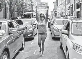  ?? AMY DAVIS/BALTIMORE SUN ?? Kahi Fraser, an employee at BCCC, marches between two long lines of cars stopped on E. Baltimore Street for a protest outside the William Donald Schaefer building.