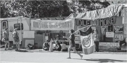  ??  ?? A woman walks with an American Indian Movement flag at Camp Cloud near the entrance of the Kinder Morgan Trans Mountain pipeline facility in Burnaby on Saturday.