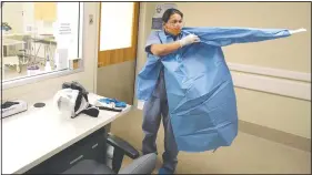  ?? (AP/Ted S. Warren) ?? Dr. Nicole Yarid, an associate medical examiner for King County in Washington, puts on a gown Tuesday as she demonstrat­es the protective equipment she uses to do autopsies on people who have died from covid-19 related complicati­ons at the Medical Examiner’s office in Seattle.