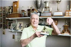  ??  ?? Wes Young, 85, poses with one of his hole-in-one trophies next to his golf trophy collection at his home in Roxboro on Saturday.