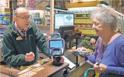  ?? KARL MERTON FERRON/BALTIMORE SUN ?? Cashier Lester Watson looks at Ruxton resident Charlotte "Penny" Owen purchase groceries at the Ruxton Graul's Market in April.