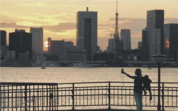  ??  ?? : A woman takes a photograph of the skyline at sunset near the Olympics athletes village in Tokyo ahead of the Games, which start on Friday