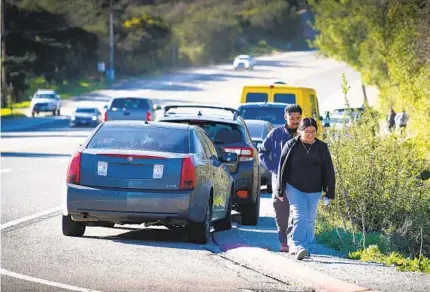  ?? HOWARD LIPIN PHOTOS FOR THE U-T ?? Pedro Avendano and Arcelia Dominguez, both from Oceanside, walk next to parked vehicles along the shoulder of state Route 67 on their way to the trailhead for Mount Woodson.
