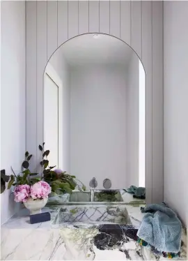  ??  ?? POWDER ROOM The Ice Green marble reigns supreme in the home’s luxurious powder room (above). “The fully-integrated marble washbasin has to be my favourite feature here,” says Gemma. Tapware from Reece complement­s the modern look while the timber wall arch is a shapely feature in the pared back room.
MAIN ENSUITE Above the shower is what Gemma describes as an “enormous” skylight that allows daylight to stream into the couple’s ensuite (above right), which comes complete with double basins and underfloor heating for the cooler months. “It’s such a luxury,” says Gemma of the added heating. White mosaic wall tiles provide the chic match to the Carrara marble vanity, while the sconce wall lights offer the right amount of task lighting when needed.
MAIN BEDROOM “This is our sanctuary,” says Gemma, of the couple’s retreat (right), which is a large bedroom with an original fireplace, as well as a new ensuite and walk-in robe. The grey fabric bedhead marries perfectly with the blue-green quilt and velvet cushion. A Home Republic stool from Adairs doubles as a bedside table, while the irregularl­y shaped mirror is a budget-friendly Target find.