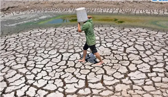  ?? A man carries a plastic bucket across the cracked bed of a dried-up pond in Vietnam’s southern Ben Tre province on March 19, 2024. Every day, farmer Nguyen Hoai Thuong prays in vain for rain to fall on the cracked dry earth of her garden in Vietnam’s Meko ??