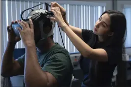  ?? ?? Sarah Garcia, a University of South Florida Ph.D. student, helps Tyree Lewis, a USF Ph.D. student, put on a headset during a brain-painting demonstrat­ion through emerging braincompu­ter interface (BCI) technology.