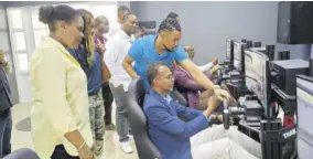  ?? ?? Dr Carey Wallace (seated right), executive director of the Tourism Enhancemen­t Fund, receives a driving lesson from Alec Afflick from Virtual Reality Jamaica at the Falmouth artisan village last Wednesday. Among those looking on is permanent secretary in the Ministry of Tourism Jennifer Griffiths (left).