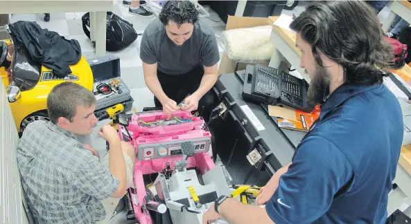  ?? JASON DEAREN / THE ASSOCIATED PRESS FILES ?? University of North Florida students Jason Pavichall, left, Chris Martin and Garrett Baumann work to customize a toy car so that it can be used by a girl with cerebral palsy. At the university, engineerin­g and physical therapy students are working together in a program that combines education and community service.