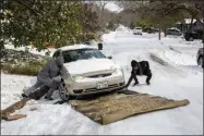  ?? BRONTE WITTPENN ?? Ivan Gonzales, left, works with his brother-in-law Gabriel Martinez to assist a motorist using a carpet up a hill along the snow-covered Cherrywood Road in Austin, Texas, on Tuesday, Feb. 16, 2021. The statewide freeze has resulted in many roads to become layered with ice and snow making several impassible and hazardous to both drivers and pedestrian­s..