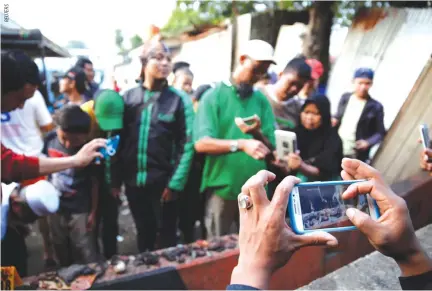  ??  ?? PEOPLE take pictures as other examine body parts found and collected around the scene of an explosion at a bus terminal in Kampung Melayu, Jakarta, Indonesia May 25.