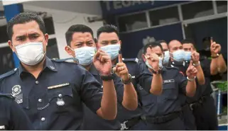  ??  ?? Leaving a mark: Police officers showing indelible ink on their fingers after early voting at the Chini police station. (Right) Workers cleaning ballot boxes in the Informatio­n Room. — Bernama
