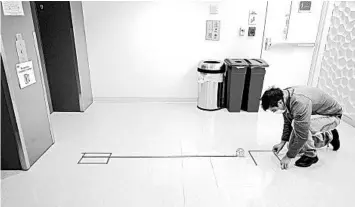  ?? STEVEN SENNE/AP ?? Kevin Gonzales places markings to promote social distancing May 21 near an elevator on the campus of Boston University.