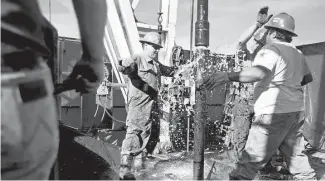  ?? James Durbin / Reporter-Telegram ?? Oil workers attach a 90-foot section of pipe onto the end of an active drill pipe on the drilling floor of a rig earlier this year in Midland County in West Texas.