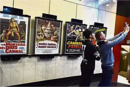  ?? — AFP ?? Wonderful disasters: Cinema-goers taking a wefie beside posters advertisin­g ‘trash movies’ in the entrance of a cinema participat­ing in the sixth edition of the CutreCon festival in Madrid.