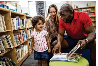  ?? TAMIR KALIFA / AMERICAN-STATESMAN ?? Lola Aladeniyi, 3, reads a book with her parents, Ron and Keri Aladeniyi, in the newly renovated library at Winn Elementary School. The East Austin school is being converted into the district’s first Montessori school, and the Aladeniyis hope to enroll...