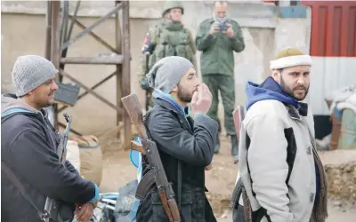  ?? — Reuters ?? Rebel fighters stand in line past Russian soldiers (back) as they wait to evacuate the besieged Waer district in the central Syrian city of Homs, after an agreement was reached between rebels and Syria’s army on Saturday.