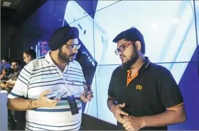  ?? BLOOMBERG ?? An attendee ( left) speaks to a representa­tive at the launch of the Xiaomi Corp MI 5 smartphone in New Delhi. Foxconn Technology Group began assembling Xiaomi’s first made-in-India smartphone from a new plant in the country.