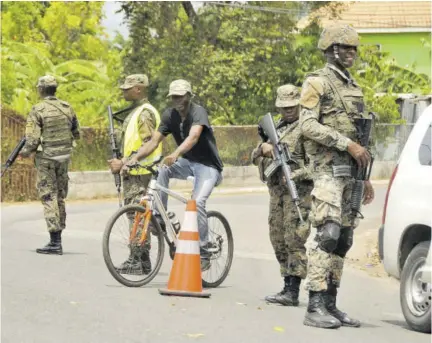  ??  ?? In this Jamaica Observer file photo, a cyclist rides through a state of emergency checkpoint manned by Jamaica Defence Force soldiers in Clarendon.